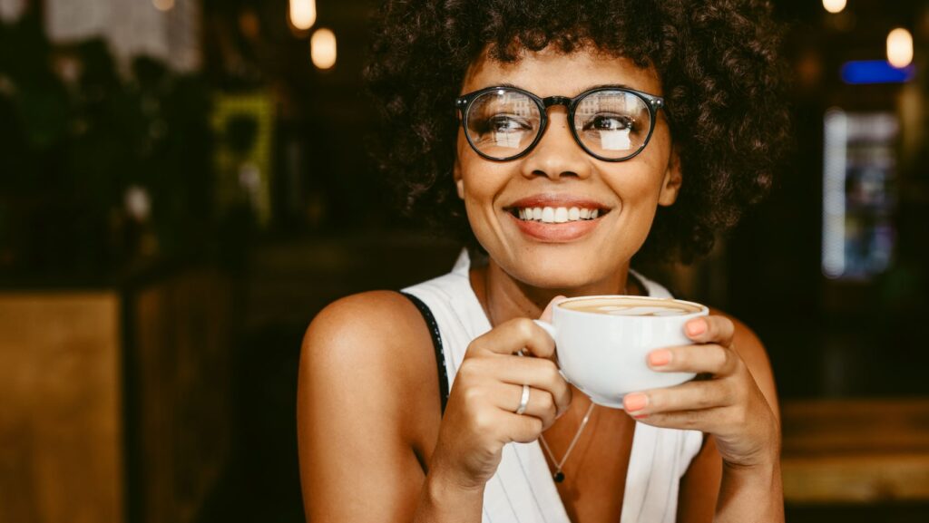 A woman smiling and drinking a cup of coffee.